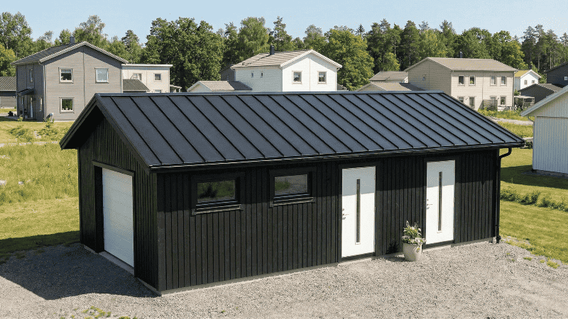 Attefallsgarage med lägenhet och toalett: mörk träbyggnad med dubbeldörr och fönster.