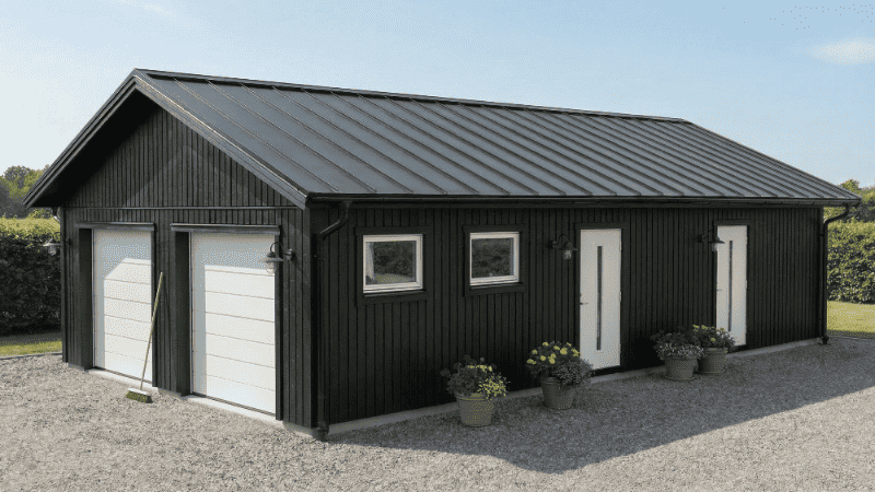 Dubbelgarage med bostadshus, mörk fasad, vita garageportar och fönster, sadeltak
